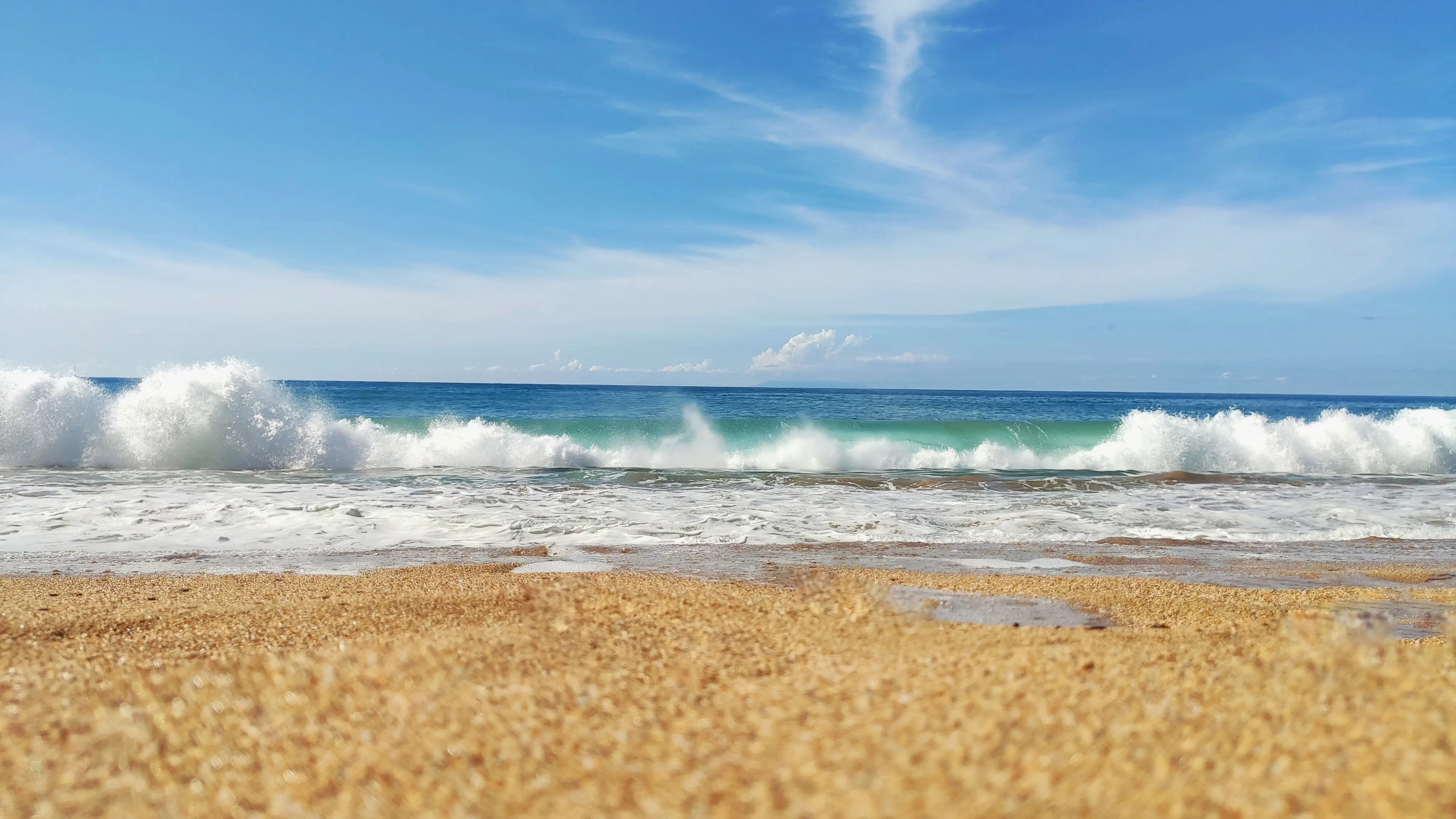 Vagues douces se déployant sur le sable doré au lever du jour, écume fine, lumière dorée